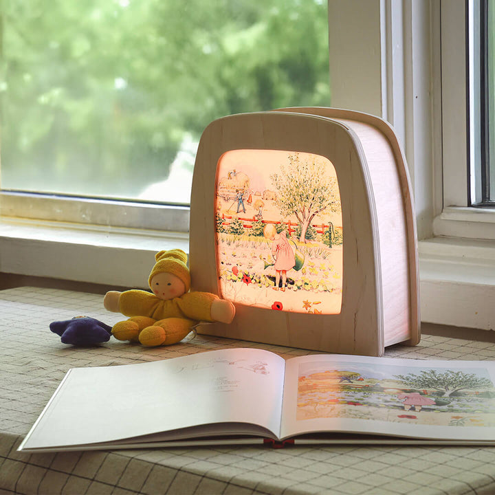 Children's book with a light-up Toverlux lamp next to a plush toy on a windowsill.