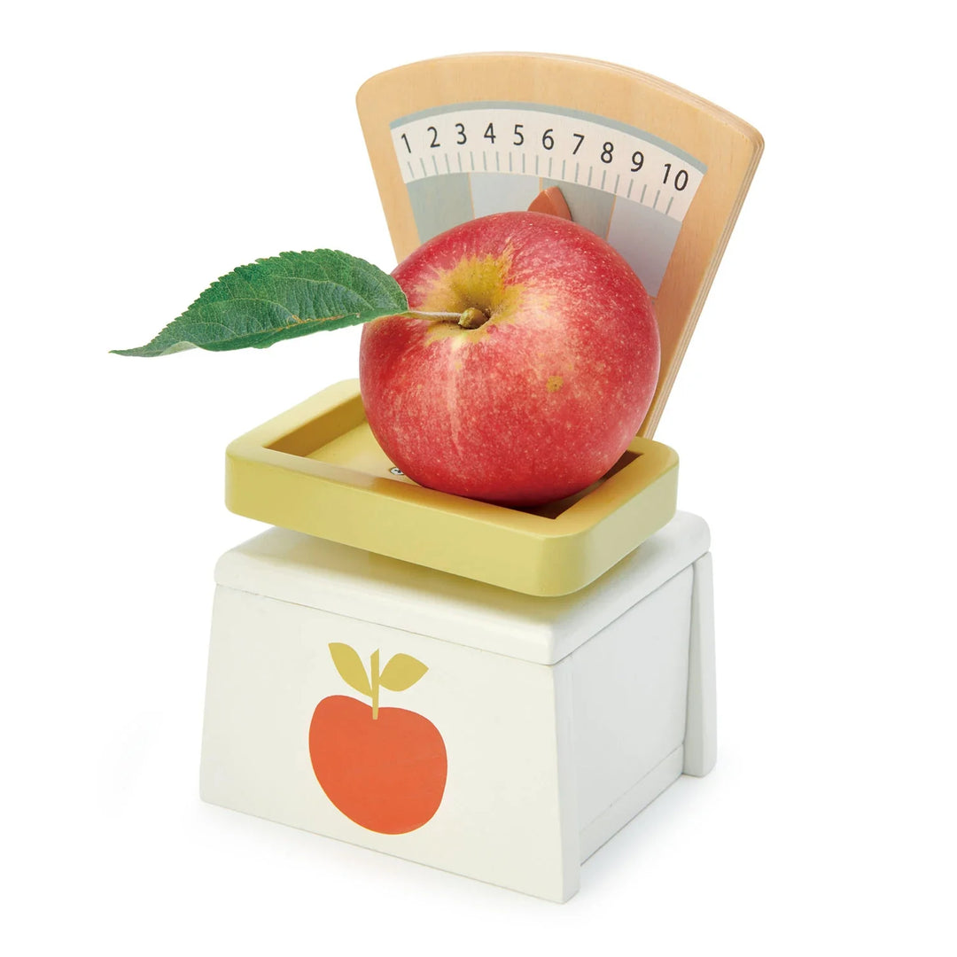 Tender Leaf Toys - Wooden Play Market Scale with numbered dial, weighing tray, and apple detail, weighing a real apple - Bella Luna Toys