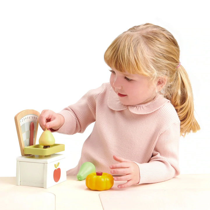 Tender Leaf Toys - Child measuring a pretend pear on the Wooden Play Market Scale - Bella Luna Toys